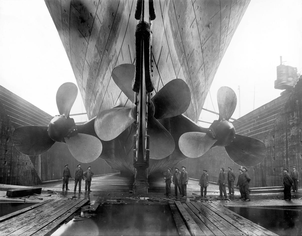 Bronze propellers of a large ship in dry dock, with shipyard workers below
